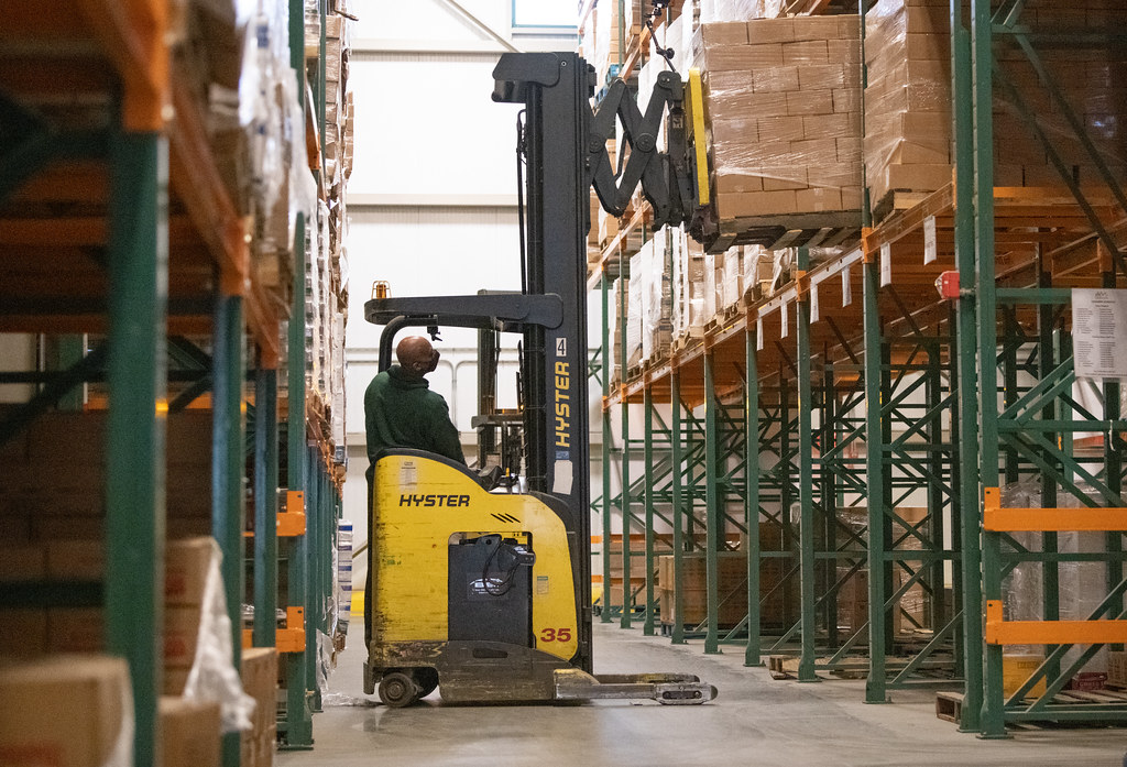 Forklift moving cartons between tall racks in a distribution warehouse
