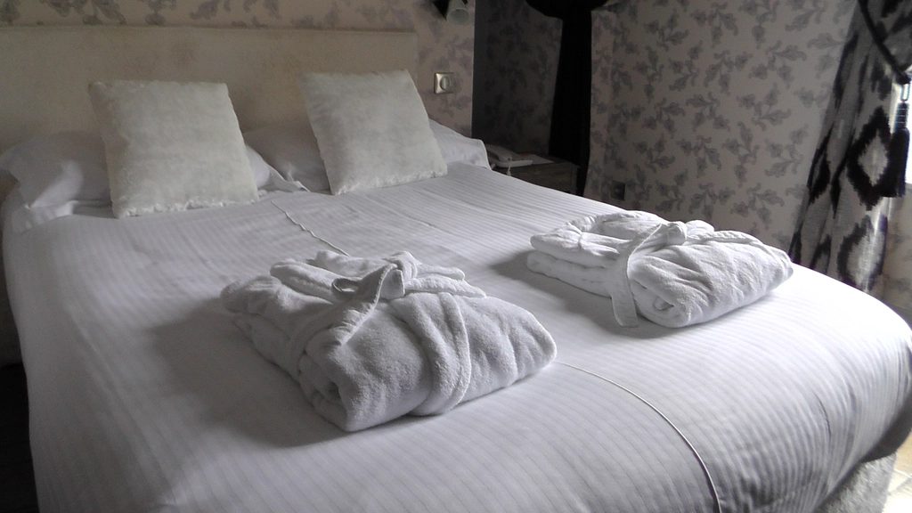 Folded white bathrobes on a made bed